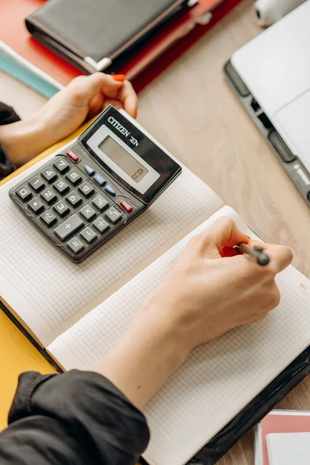 Hands using a calculator and writing figures in a notebook